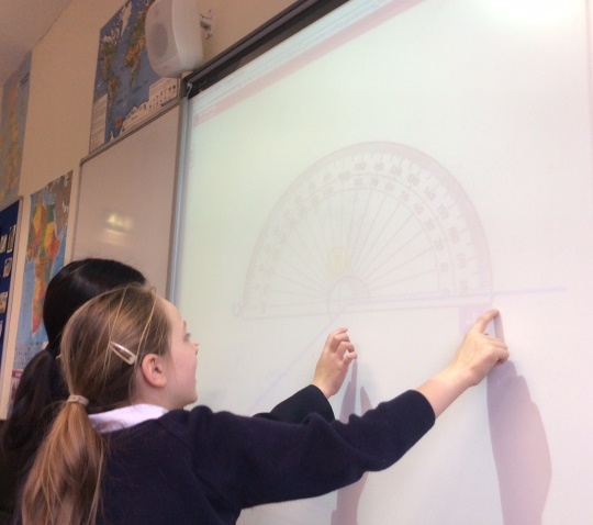 Year 5 pupils looking at white board with protractor
